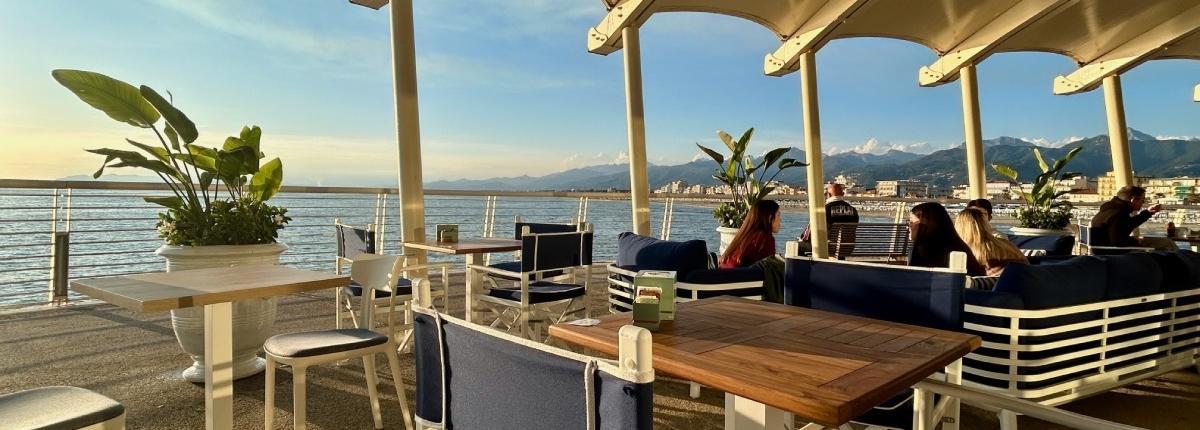 Il locale Le Grand Bleu Caffè Bistrot sul pontile di Lido di Camaiore all'ora del tramonto, il mare e le Apuane