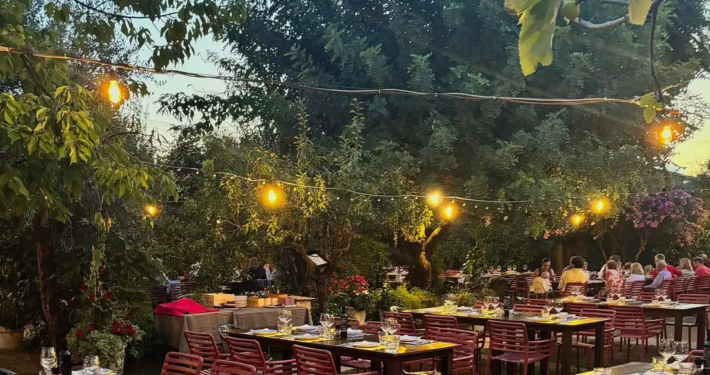 Einladender und üppig grüner Sommergarten der Osteria A’ Pagliai in der Toskana mit langen Holztischen und warmer Abendbeleuchtung, ideal für ein Abendessen mit Freunden.